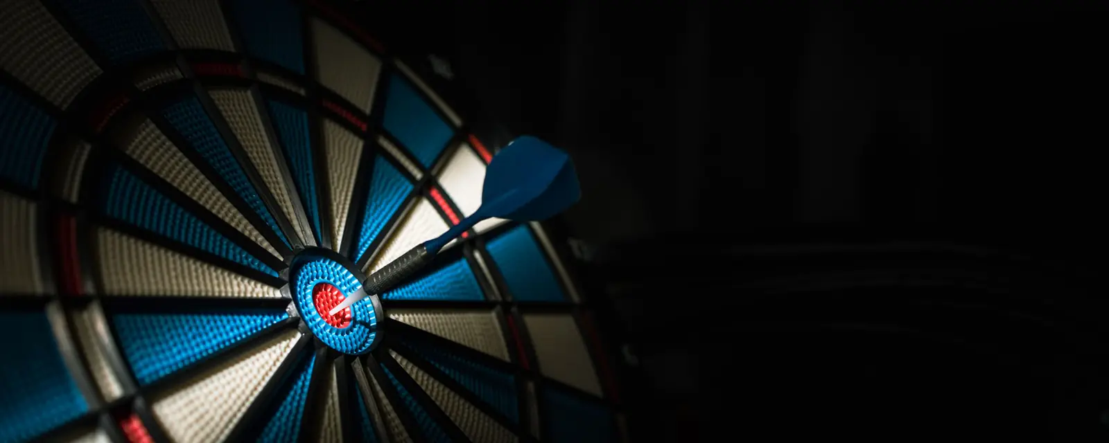 Dartpfeil steckt nahe dem Bullseye einer beleuchteten Dartscheibe