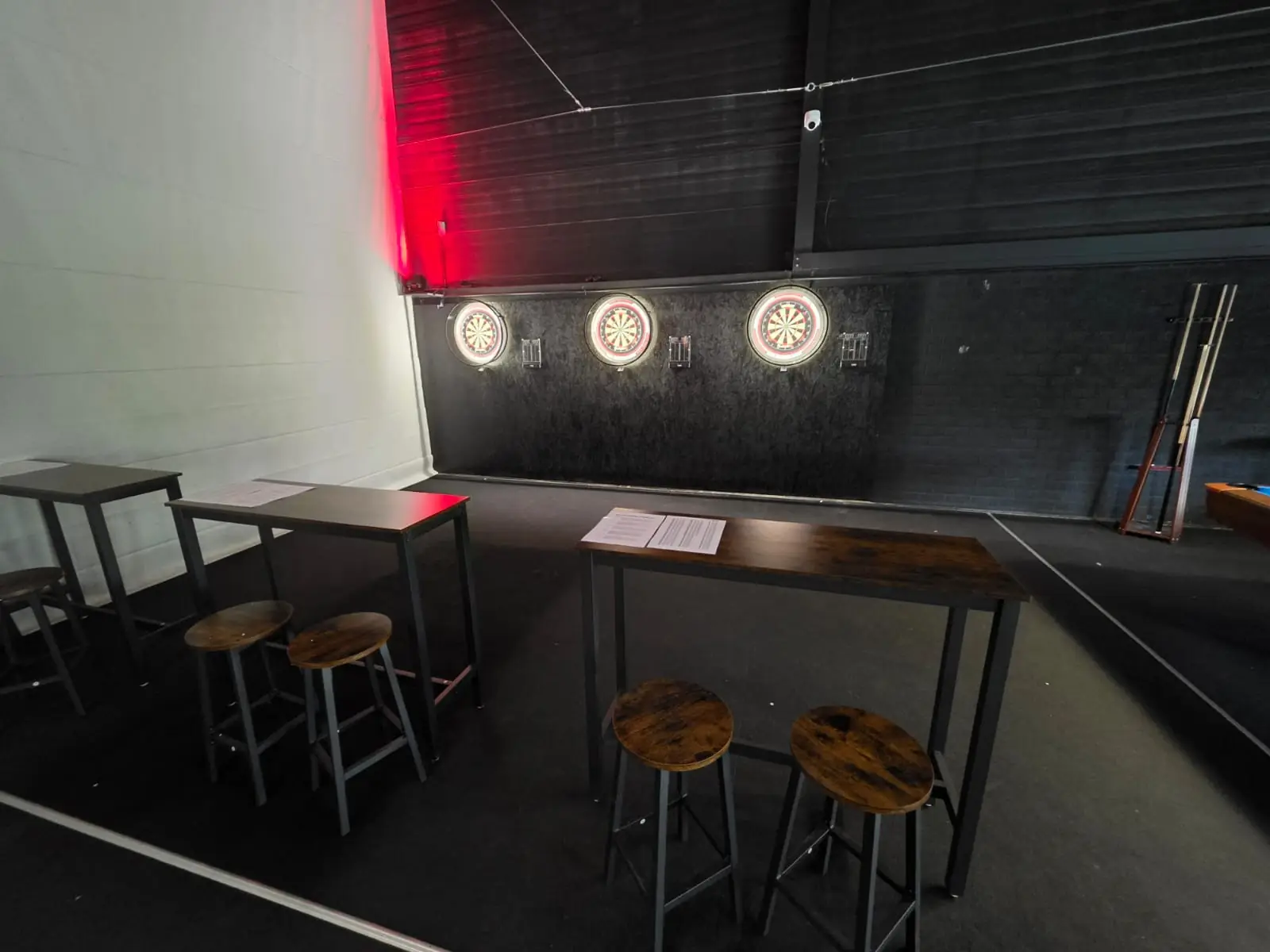 Drei Steeldartscheiben an der Wand, davor Stehtische mit Hockern